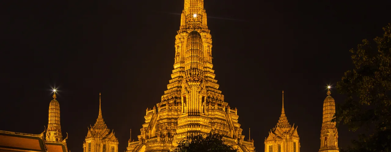 Wat Arun temple towers glowing at dusk beside the Chao Phraya River in Bangkok